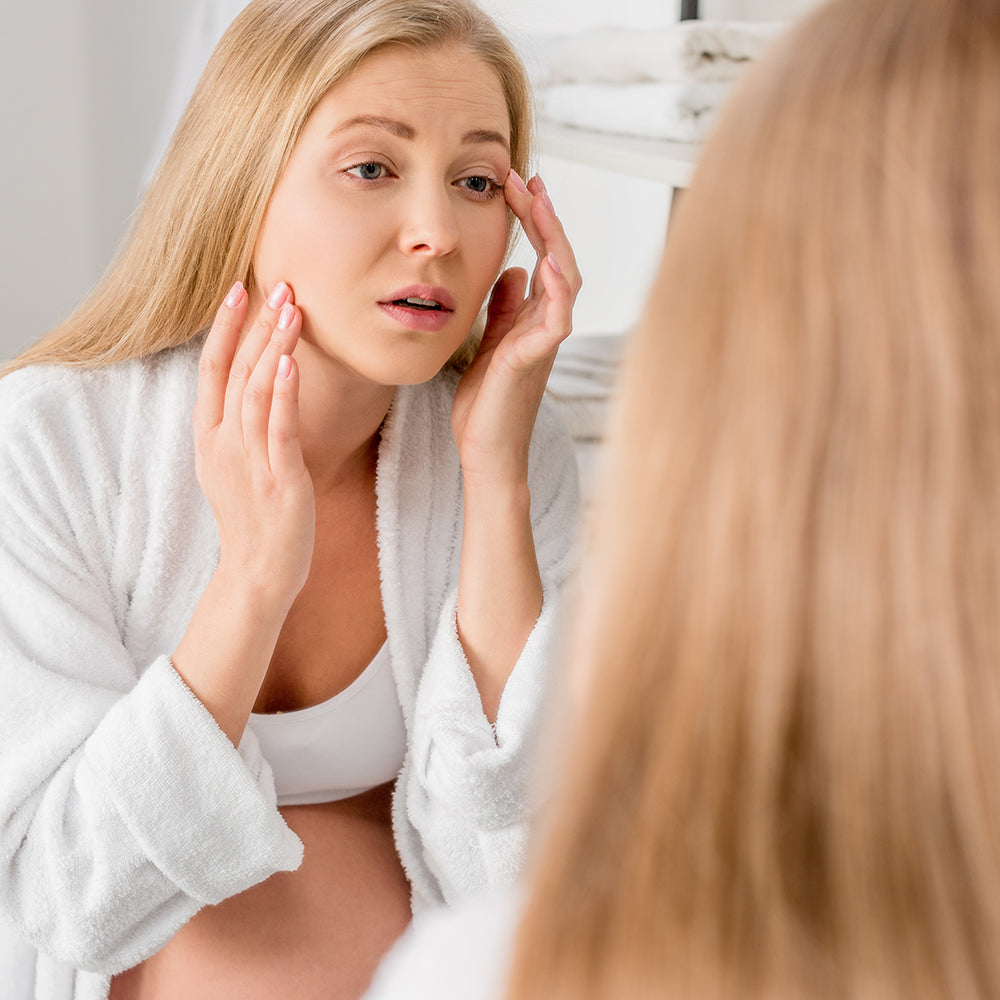 Mujer embarazada con problemas de piel y acné hormonal mirándose el rostro